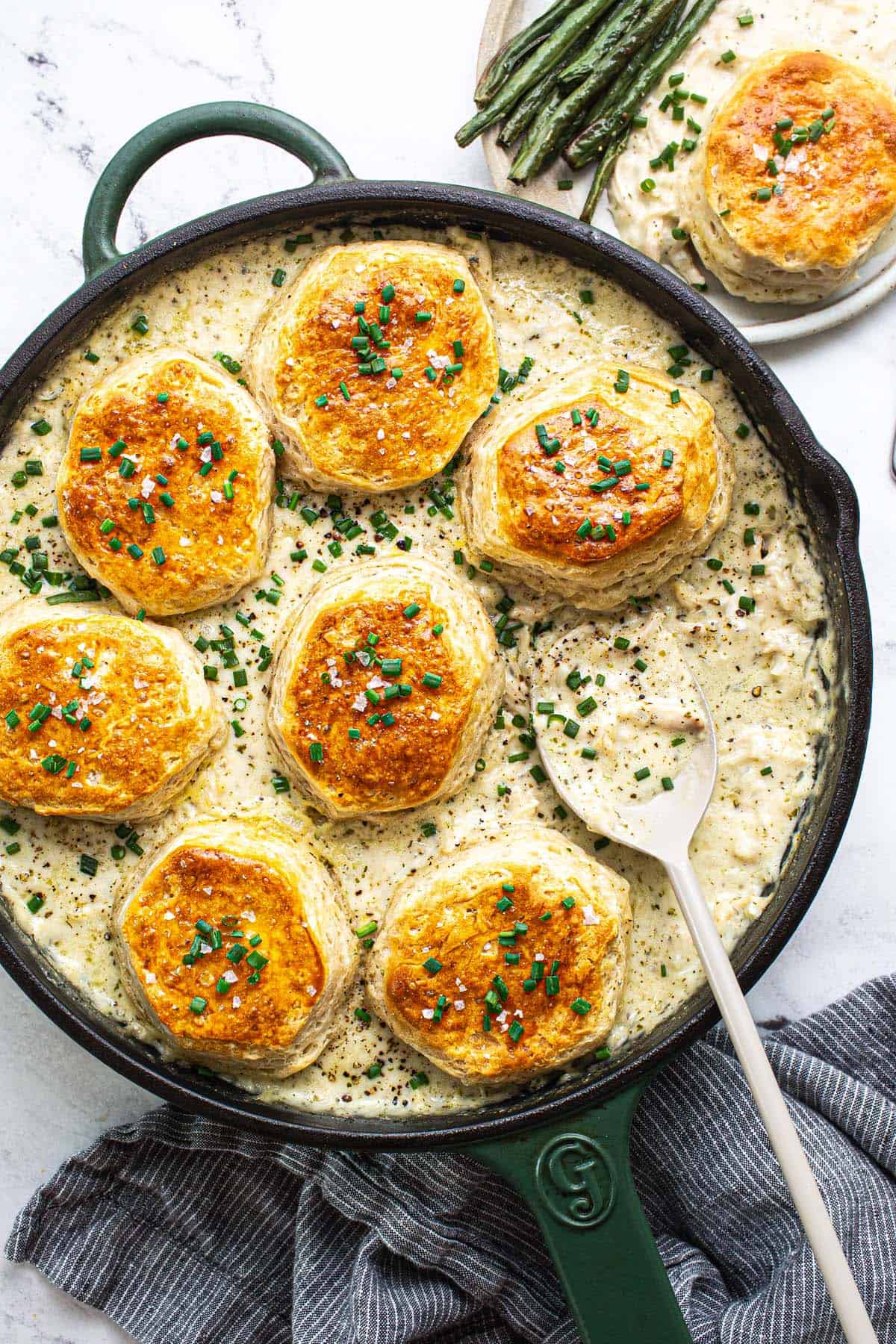 Large pan filled with creamy chicken and biscuits garnished with chives. 