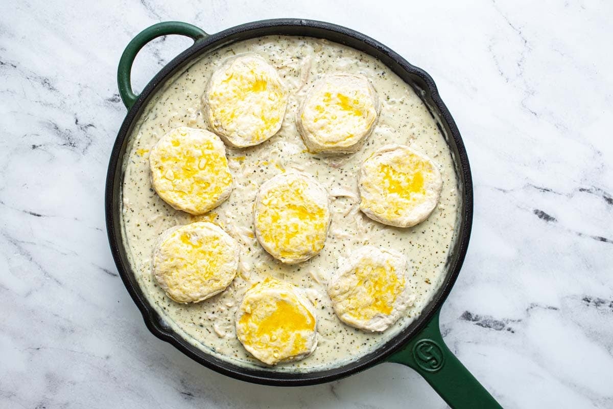 Large pan of chicken and biscuits topped with biscuits brushed with egg wash. 