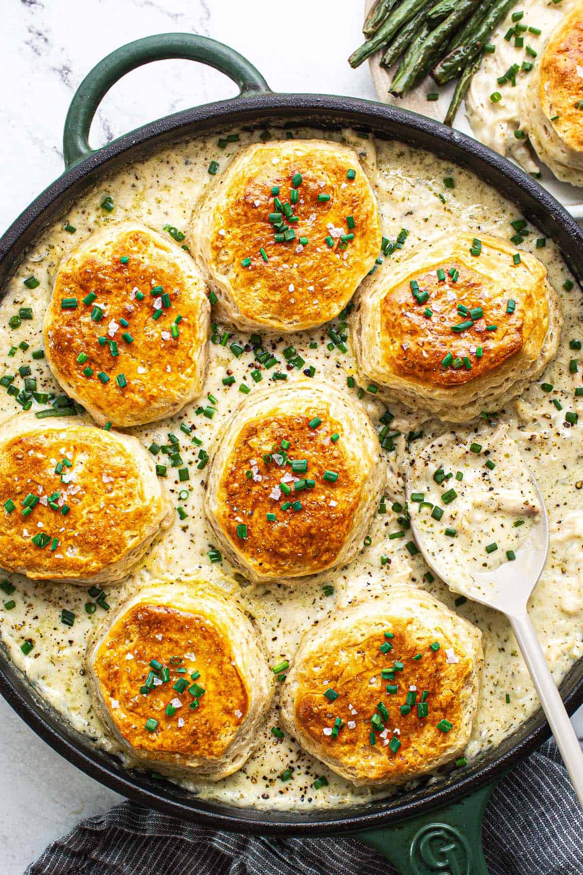 Large pan filled with creamy chicken and biscuits garnished with chives. 