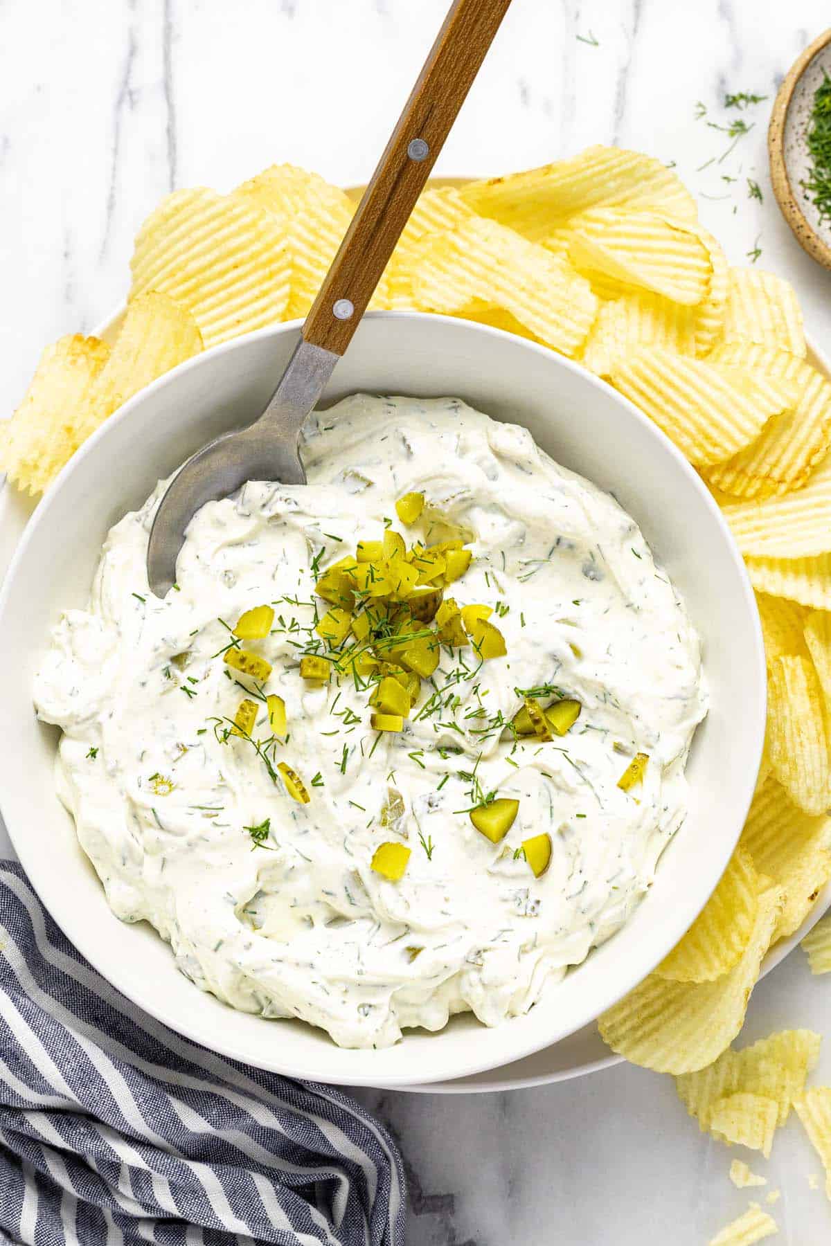 Bowl of dill pickle dip on a plate of Ruffles potato chips.