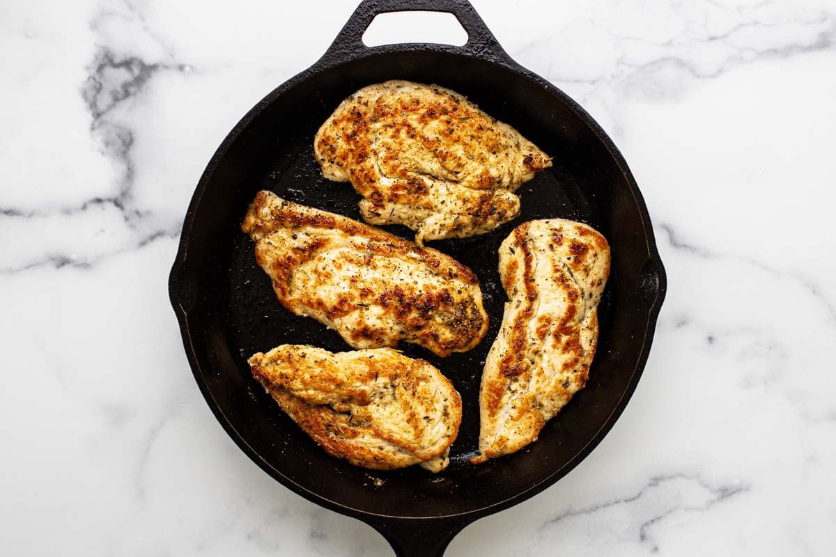 Cast iron skillet with sauteed chicken in it. 