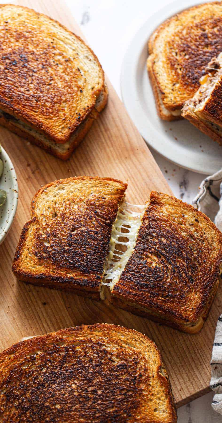 A patty melt cut in half on a cutting board with a beautiful cheese pull.