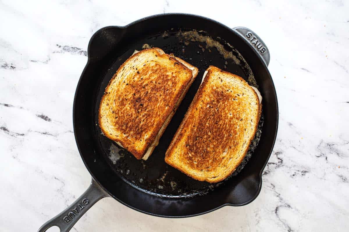 Two cooked patty melts in a cast iron pan.