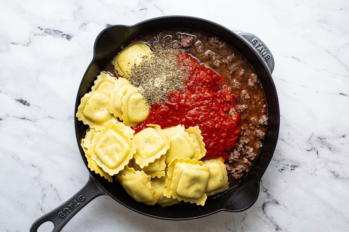 Large skillet with ground beef, red sauce, ravioli, herbs, and spices. 