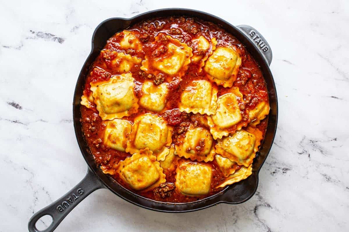 Large skillet with ravioli tossed in meat sauce. 