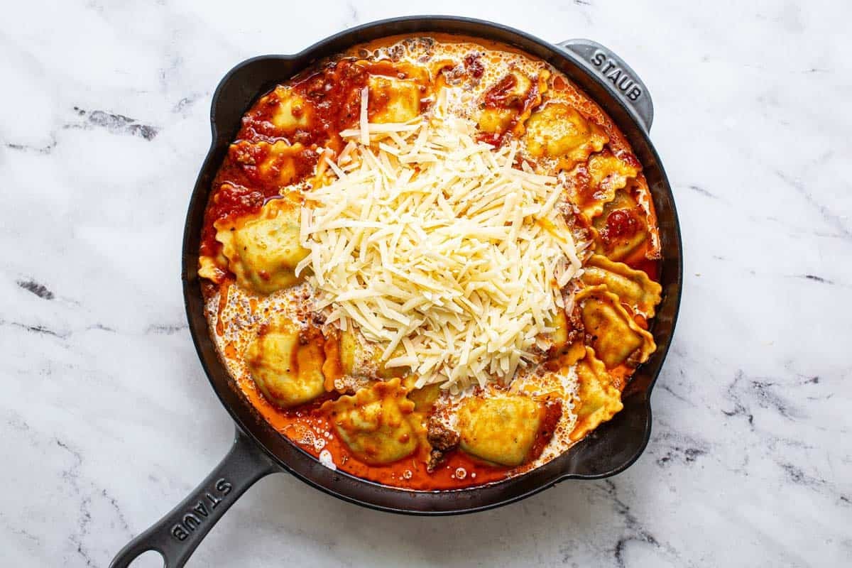 Parmesan cheese and heavy cream added to a pan of ravioli and meat sauce. 
