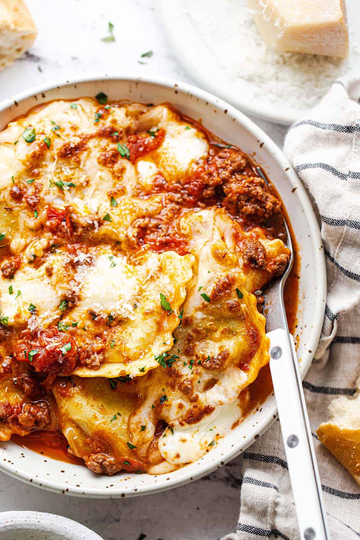 Close up shot of baked ravioli and meat sauce in a bowl with a fork. 
