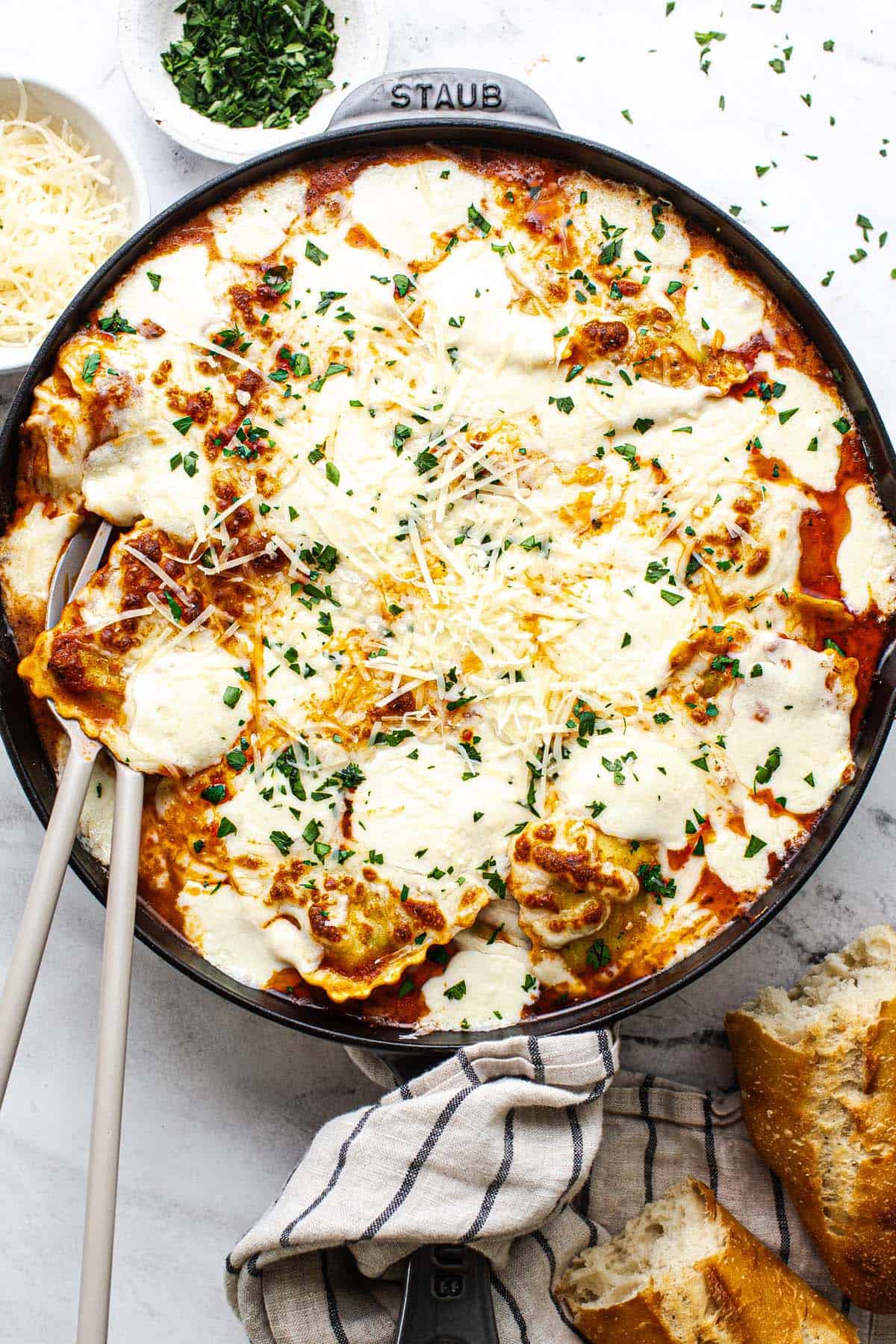 Large skillet filled with baked ravioli garnished with parsley.
