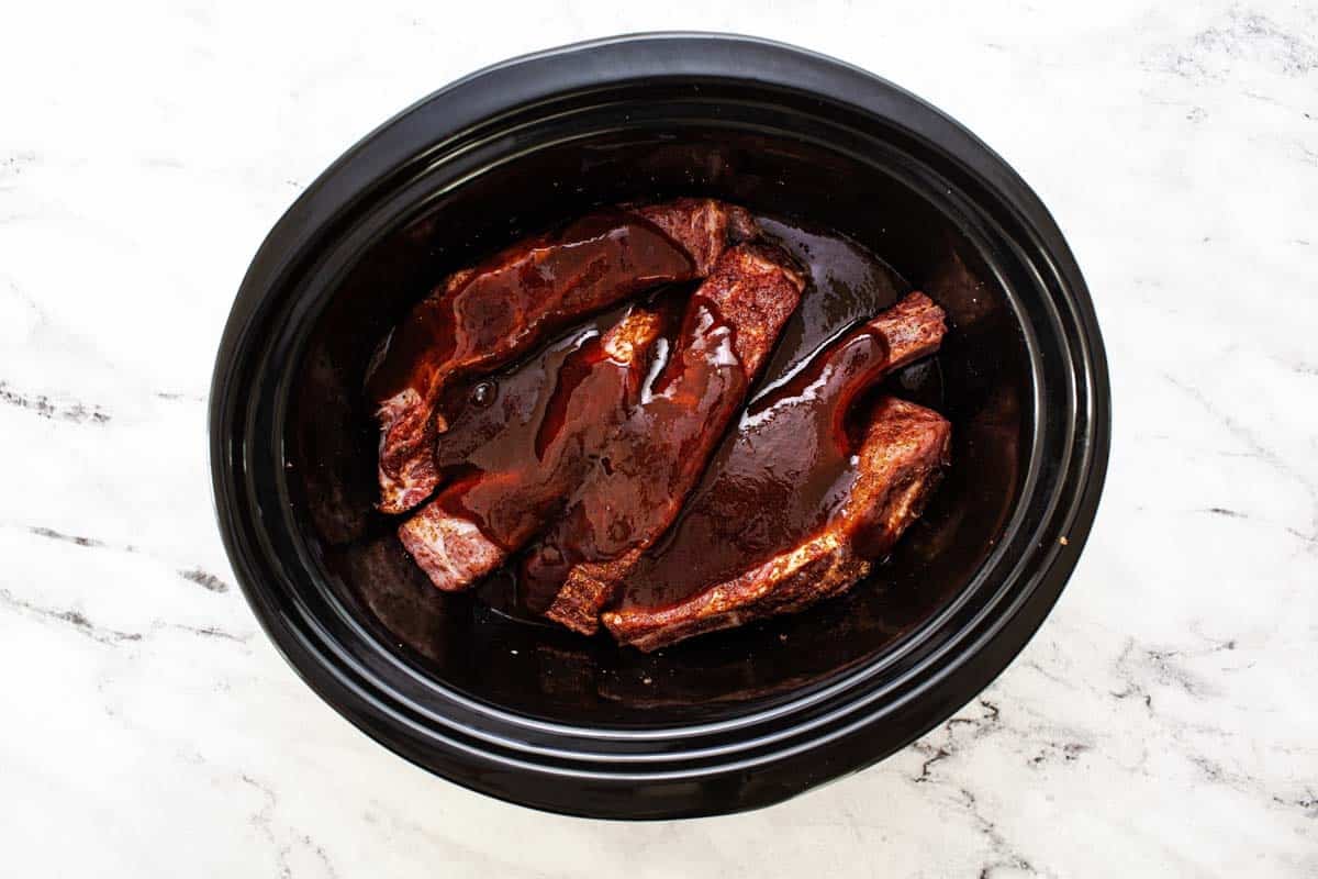 Barbecue sauce poured over pork ribs in a slow cooker. 