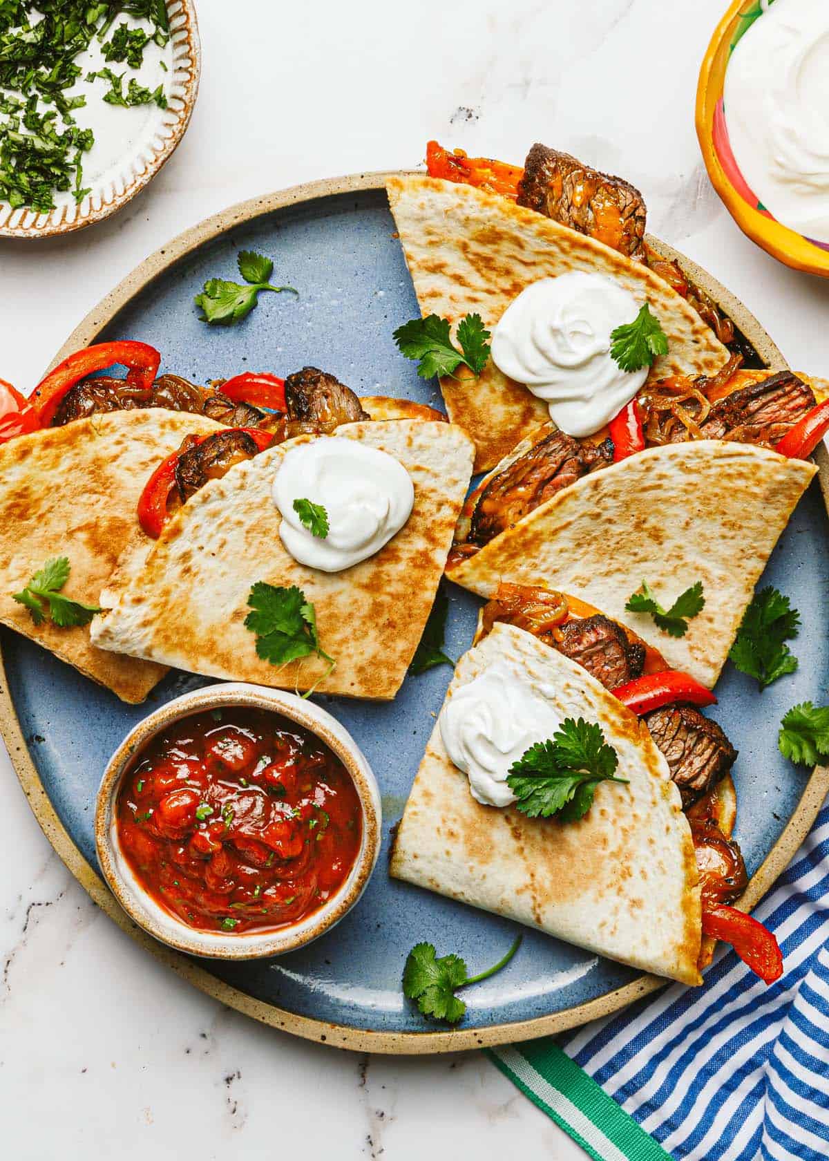 Steak quesadillas cut into quarters on a plate with salsa and sour cream. 