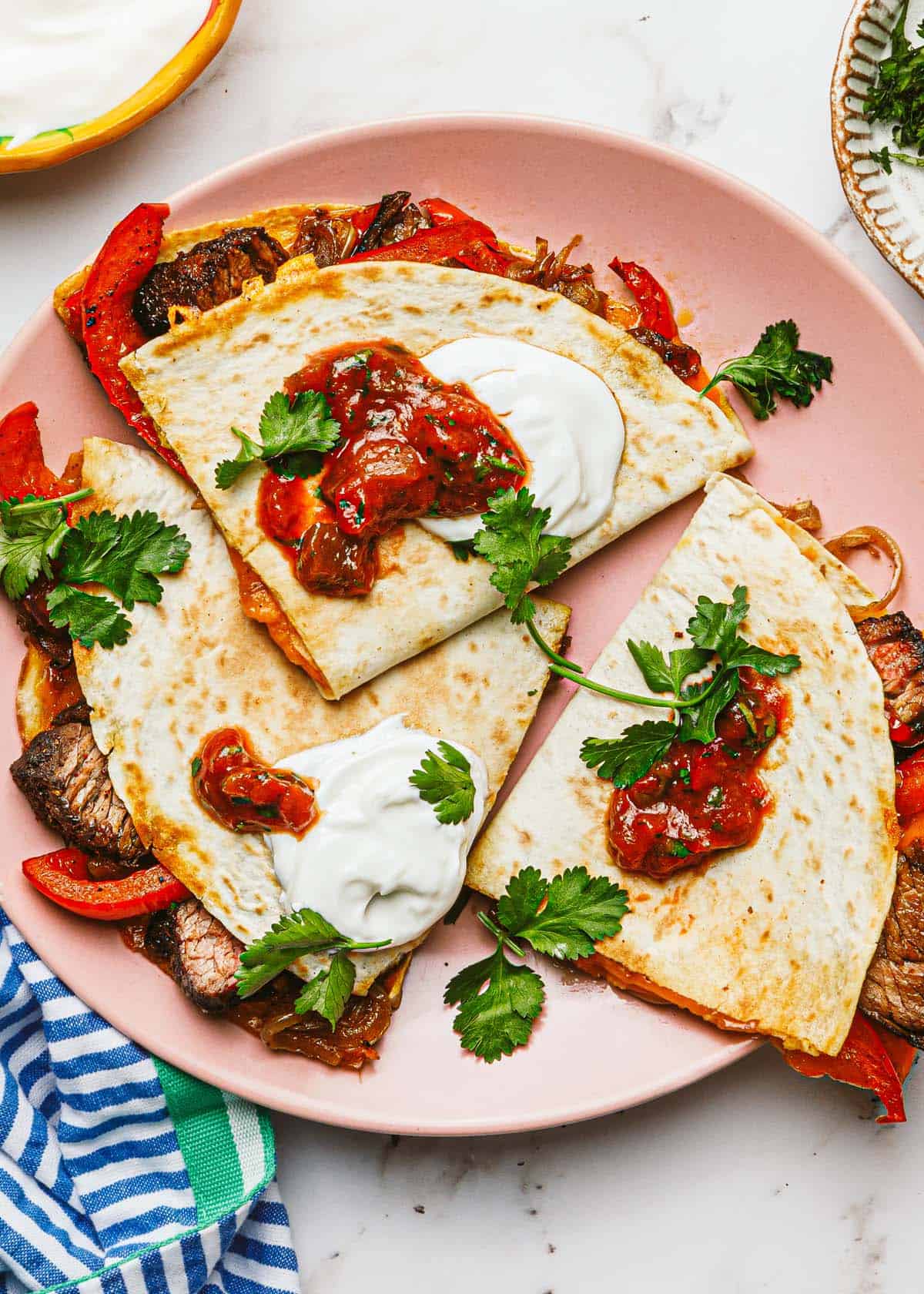 Steak quesadillas cut into quarters on a plate with salsa and sour cream. 