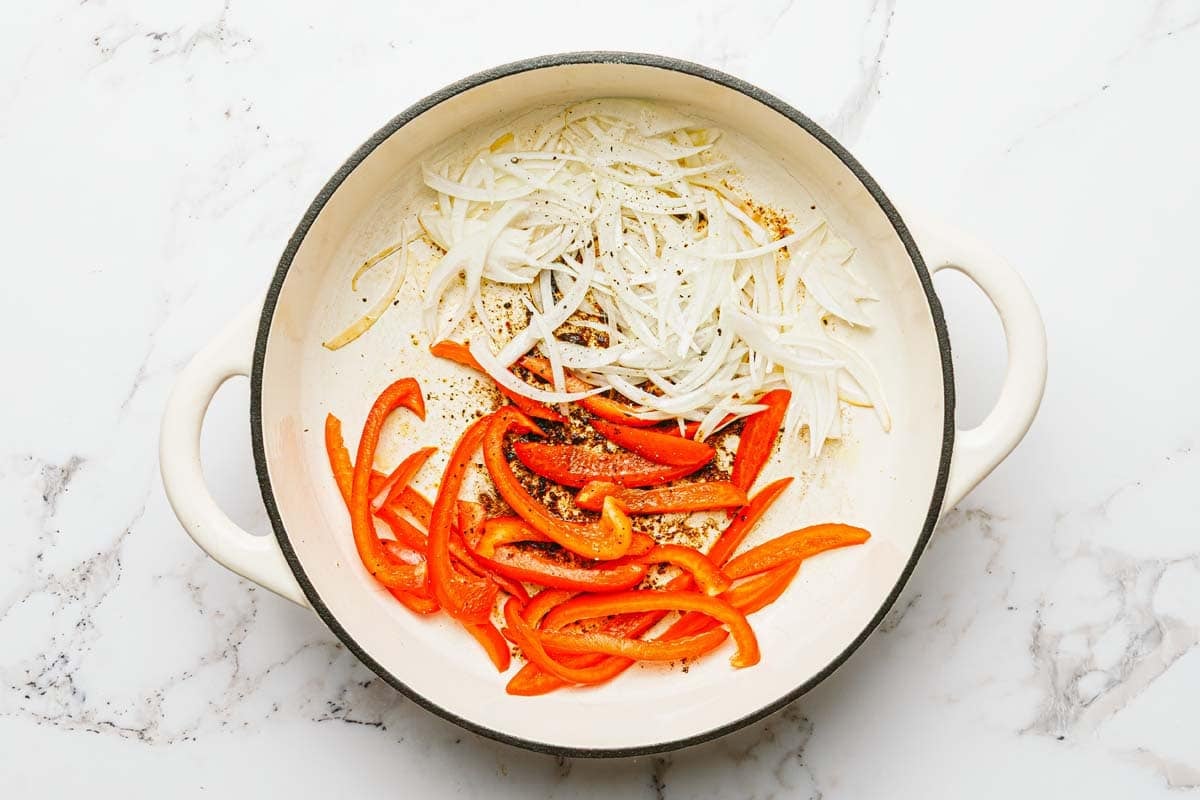 Large saute pan with sliced onion and bell pepper. 