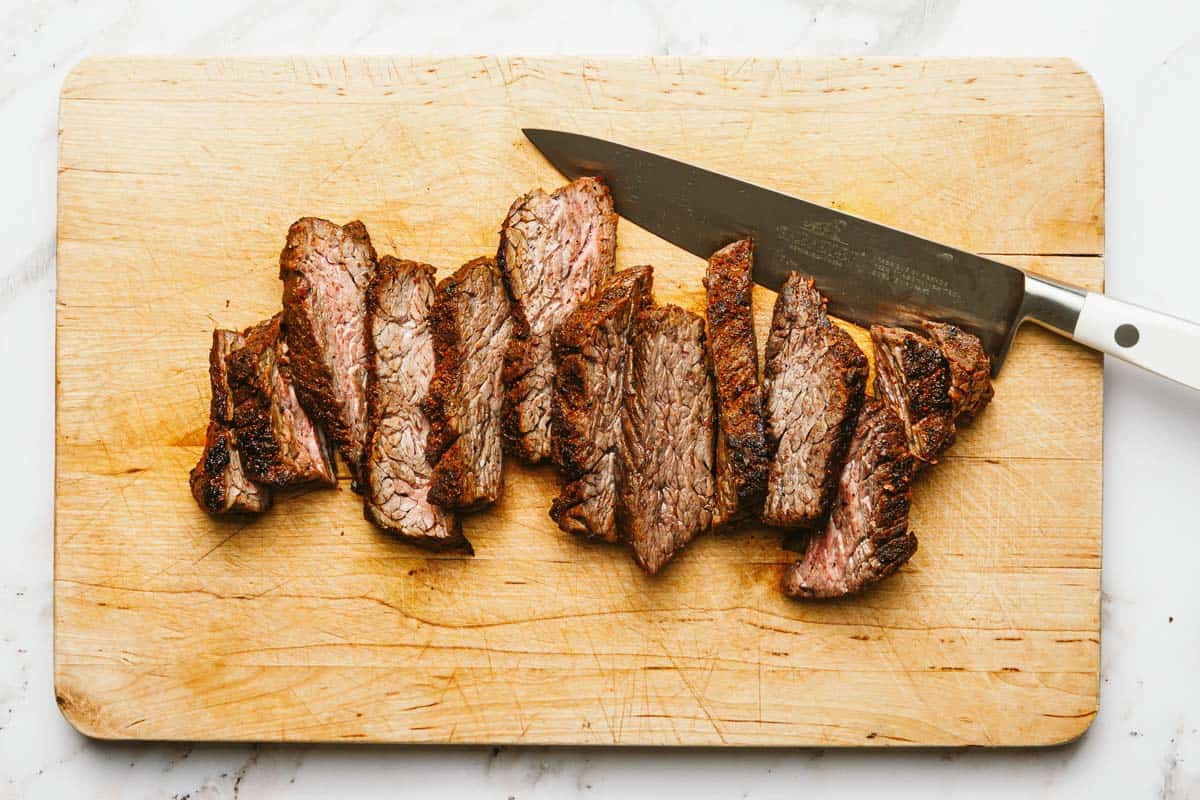 Sliced steak on a large wooden cutting board. 