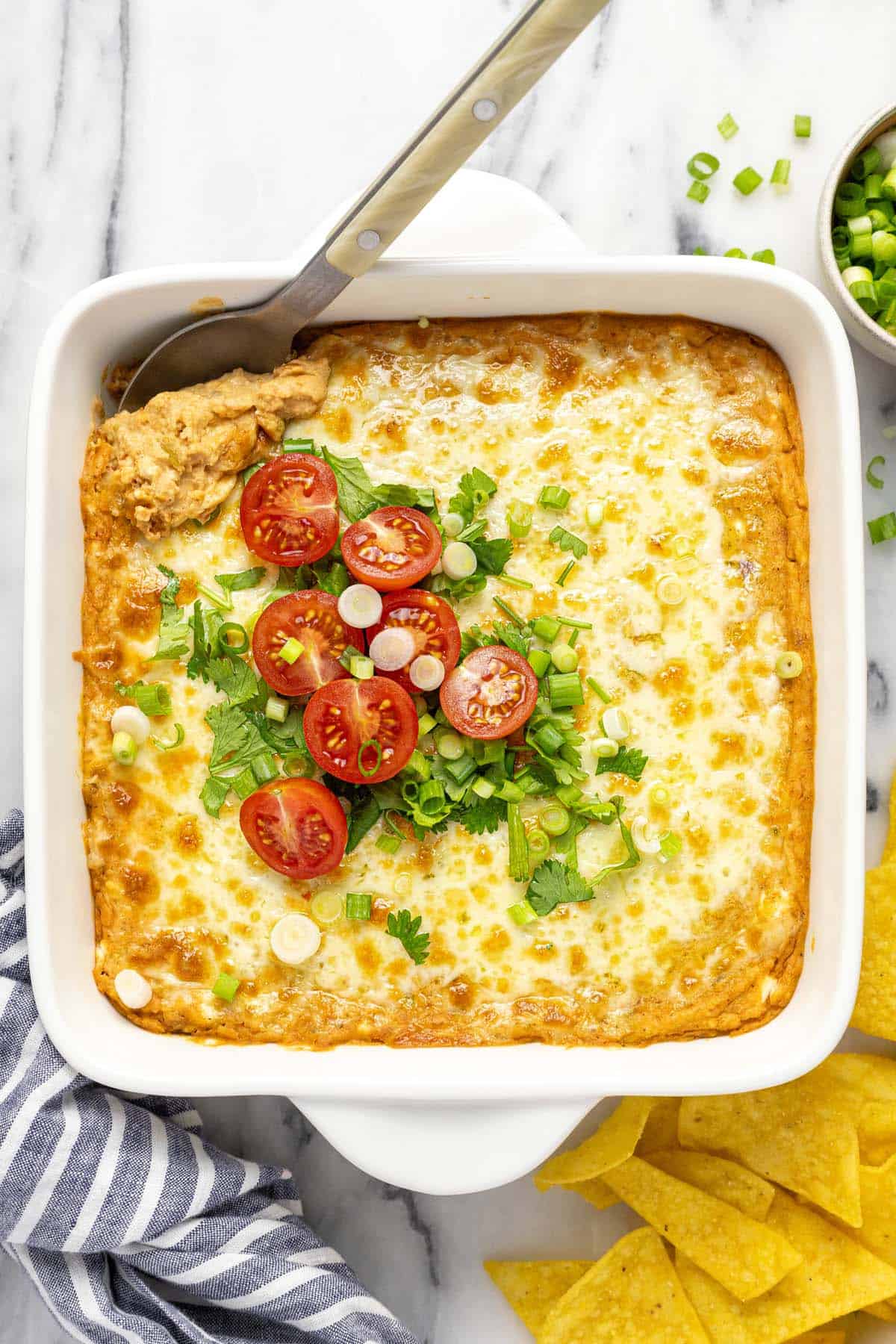 Baking dish filled with creamy bean dip topped with melted cheese, tomatoes and green onion. 