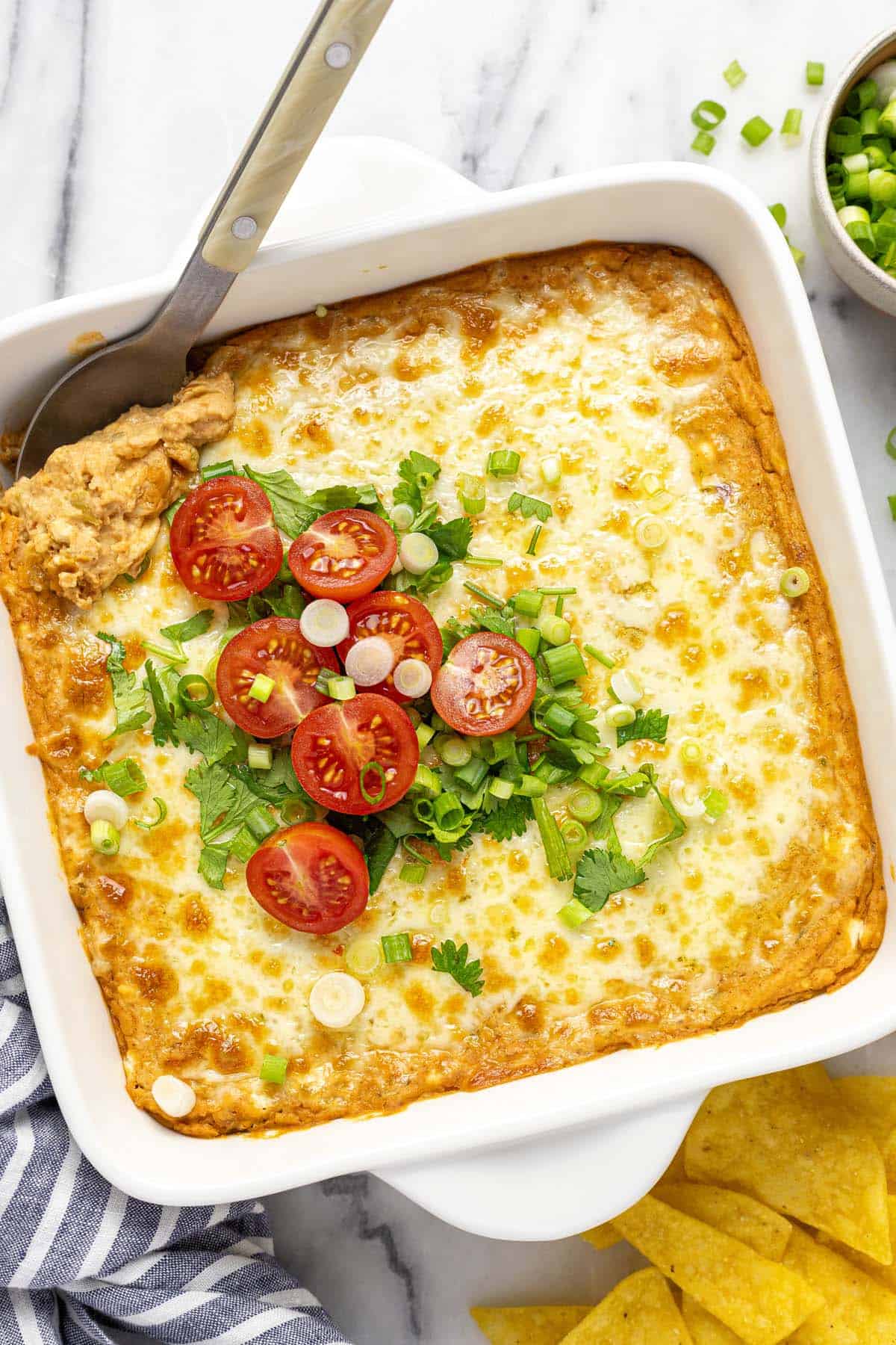 Baking dish filled with creamy bean dip topped with melted cheese, tomatoes and green onion. 