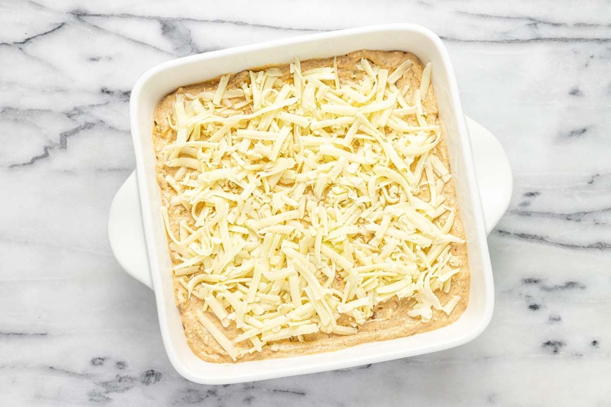 Creamy bean dip in a baking dish topped with shredded cheese. 