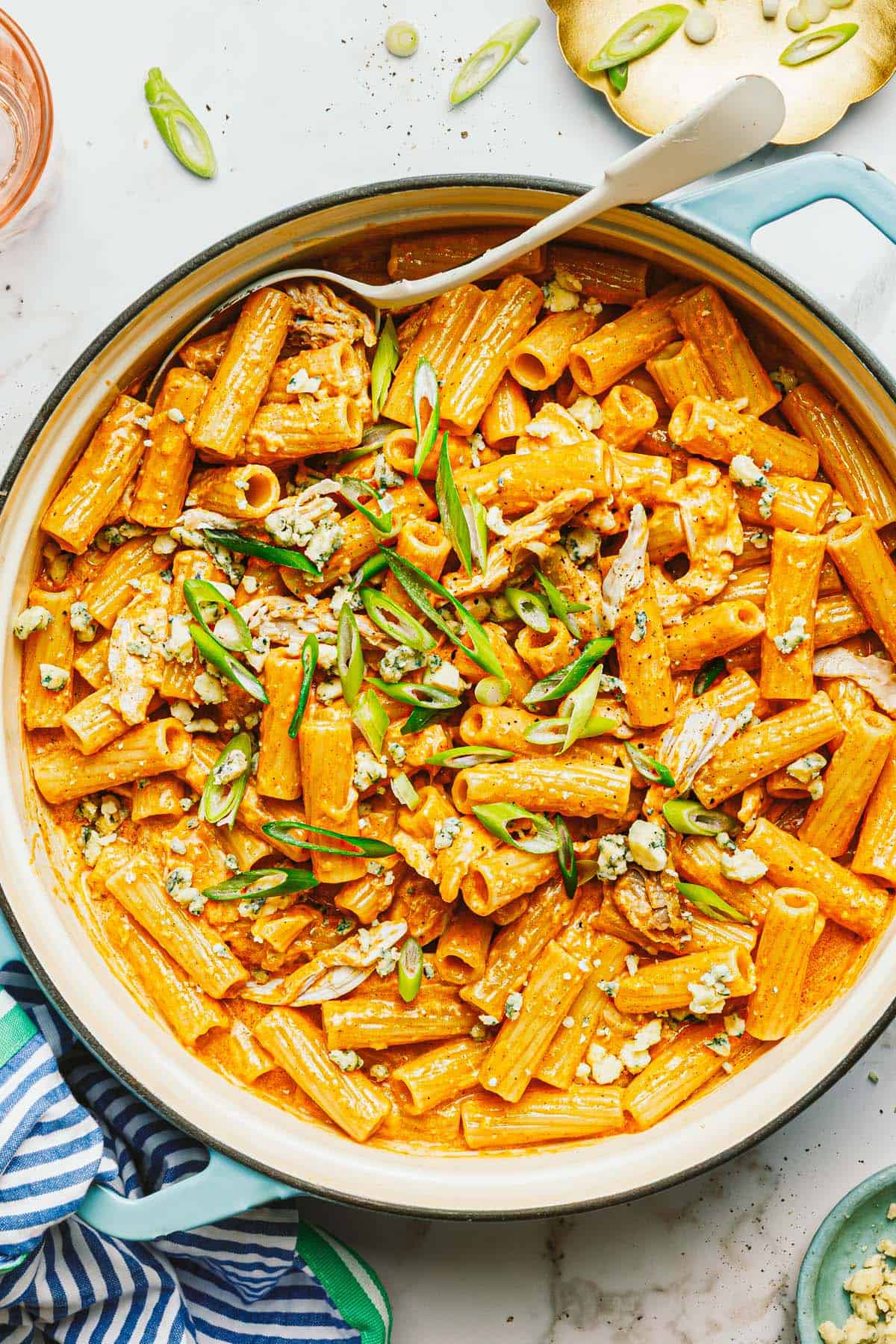 Large pan of creamy buffalo chicken pasta garnished with blue cheese and green onion. 