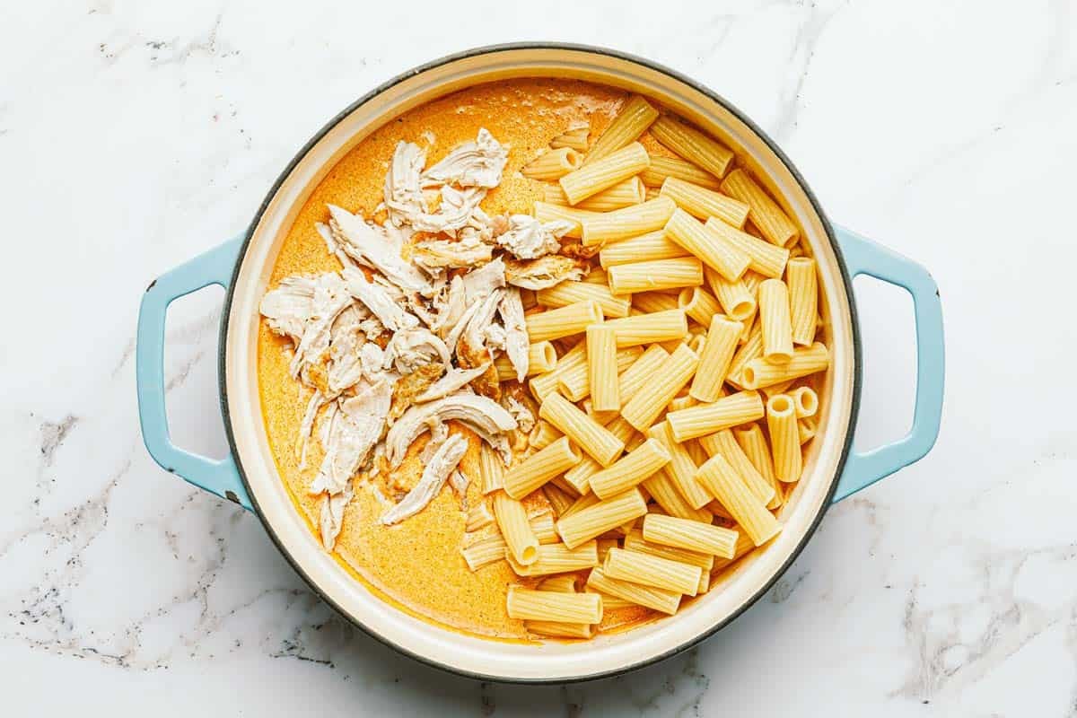 Pasta and shredded chicken added to a pan of creamy buffalo sauce. 