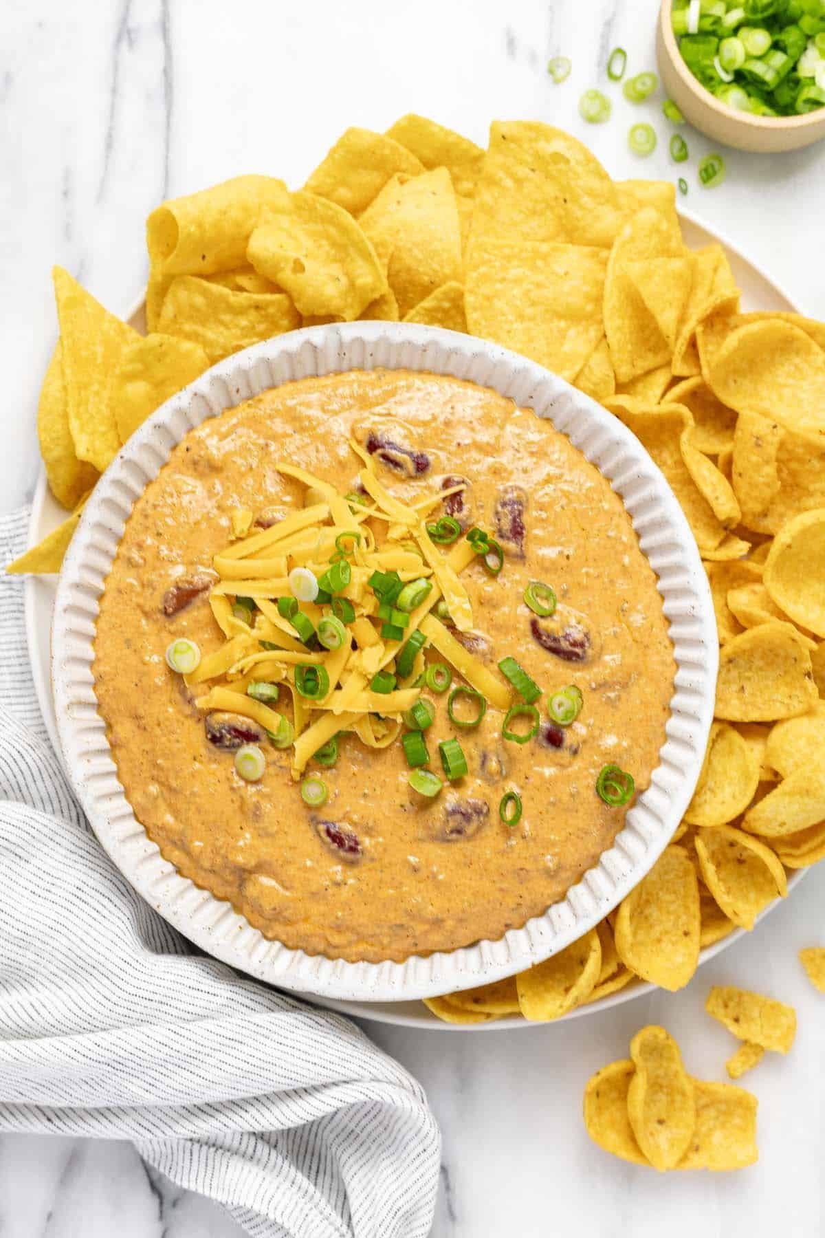 Bowl of chili cheese dip on a plate of tortilla chips and Fritos. 