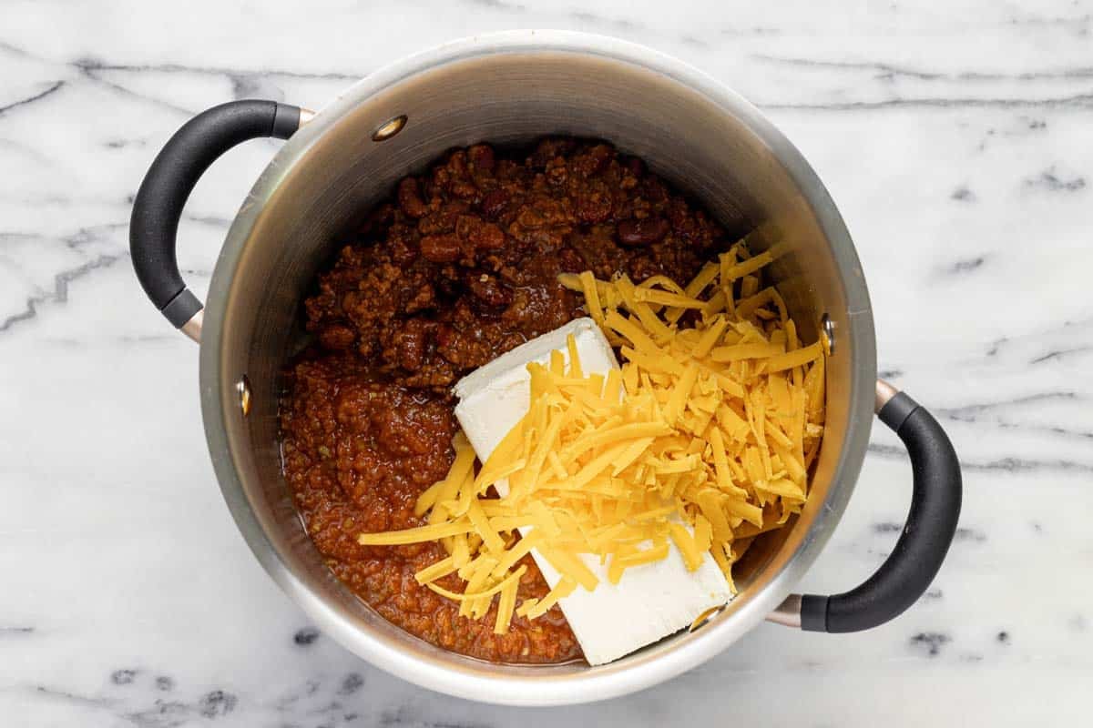 Large pot with chili, cream cheese, salsa, and shredded cheese. 