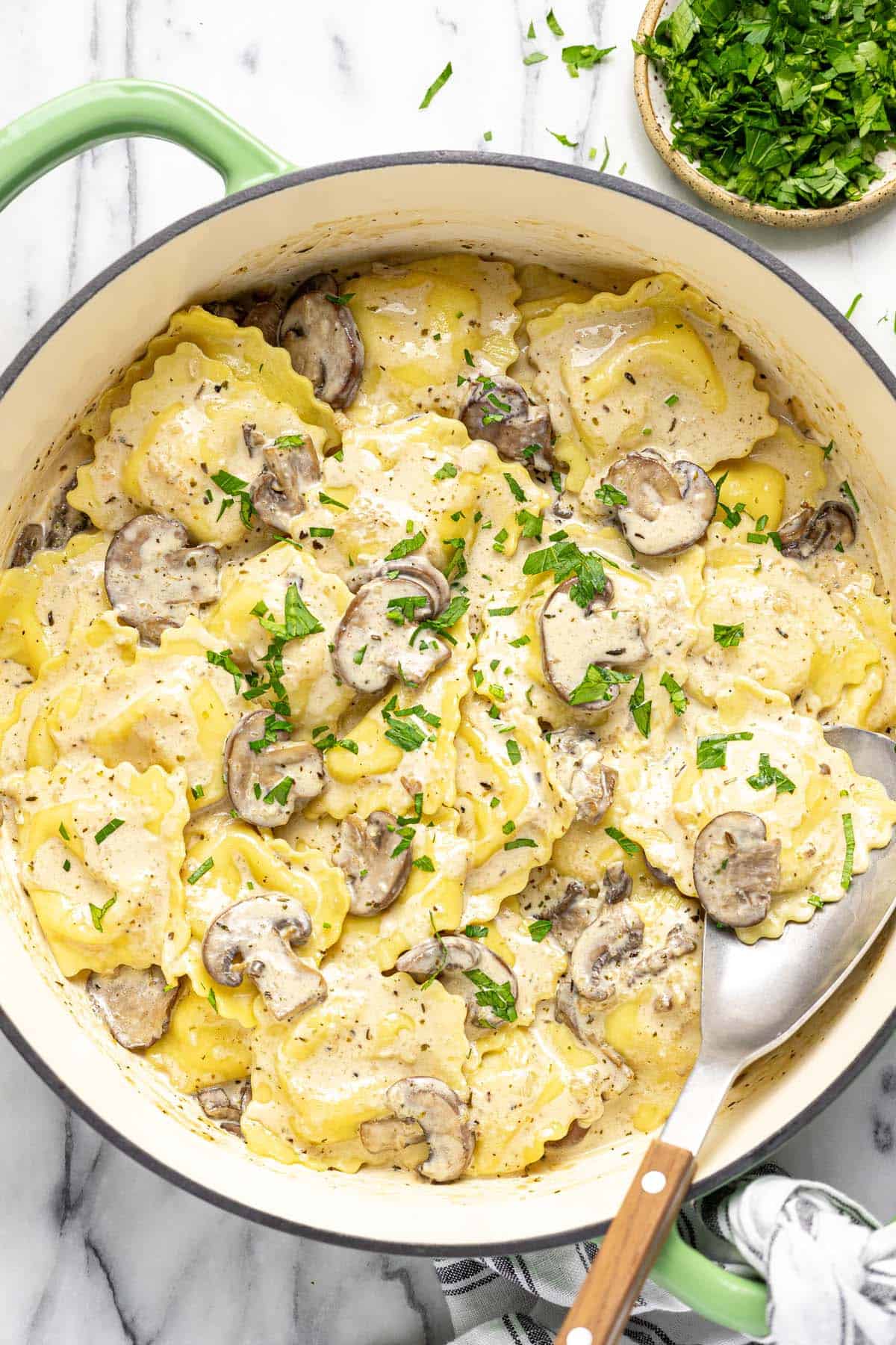 Large pan filled with mushroom ravioli garnished with parsley. 