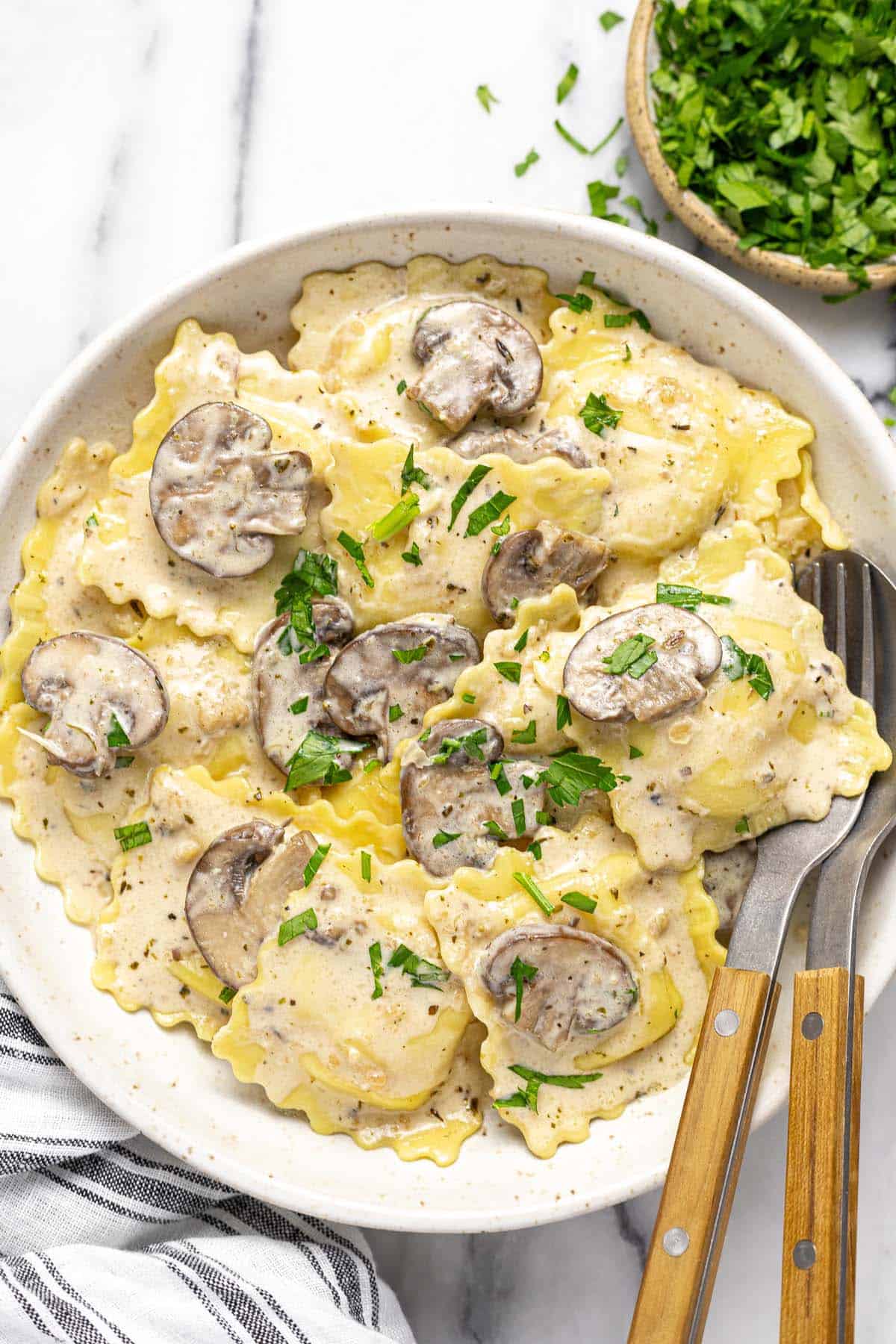 Large bowl filled with mushroom ravioli garnished with chopped parsley. 