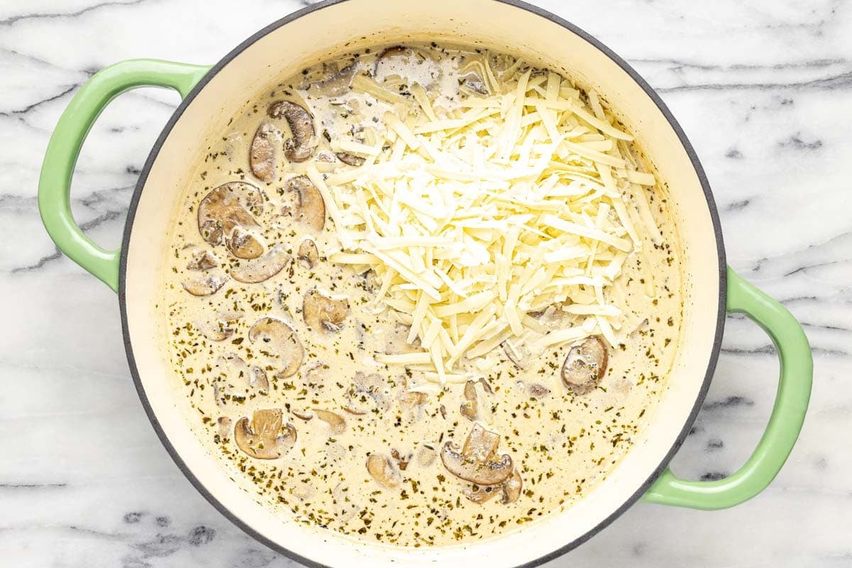 Creamy mushroom sauce in a pan with shredded Parmesan. 