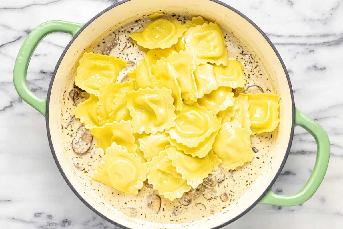 Cheese ravioli added to a pan of creamy mushroom sauce. 