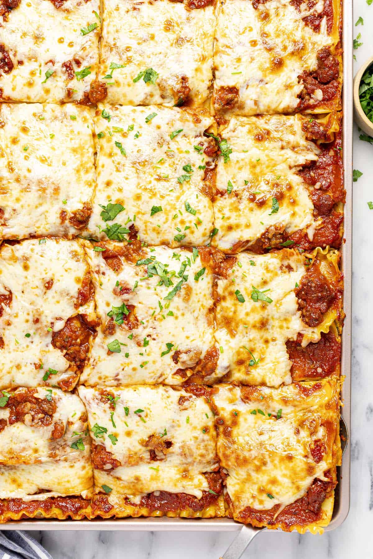 Close up of sheet pan lasagna cut into pieces and garnished with parsley. 
