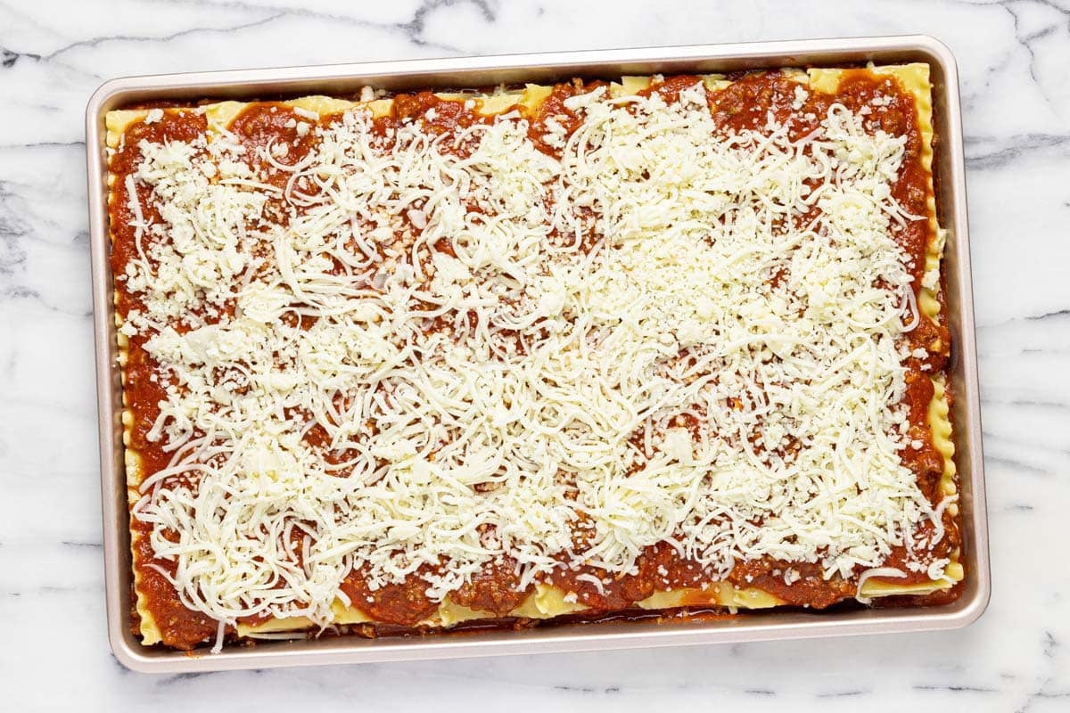 Freshly assembed sheet pan lasagna topped with shredded cheese. 