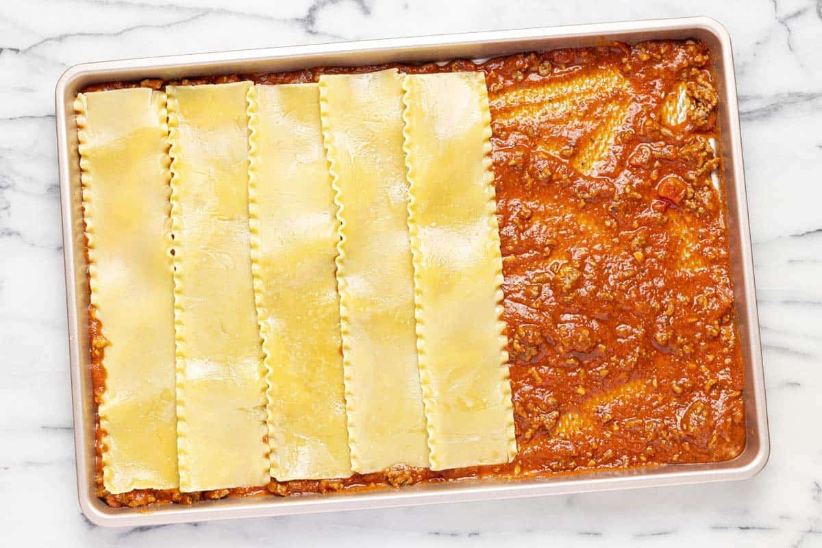 Sheet pan layered with meat sauce and lasagna noodles. 