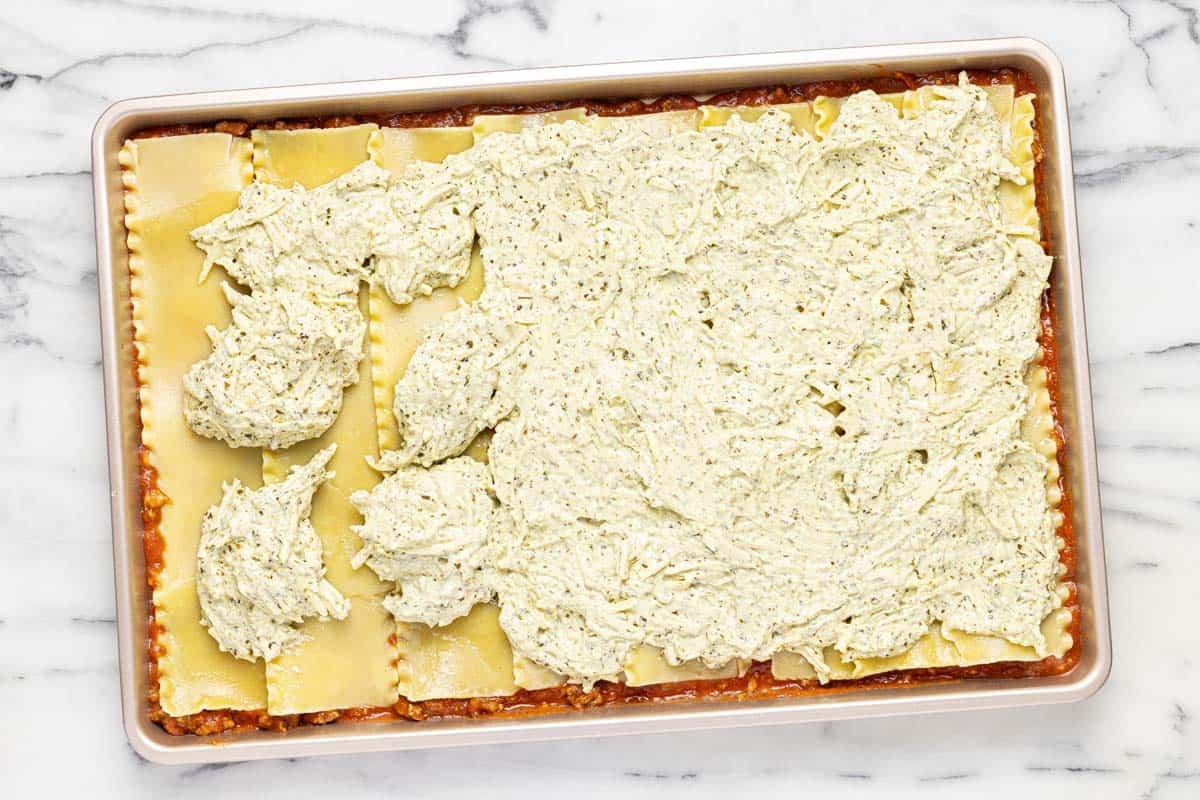 Meat sauce, noodles, and cheese filling for lasagna on a sheet pan. 