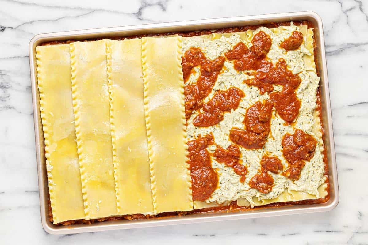 Sheet pan with layers of sauce, cheese, and noodles on a sheet pan. 