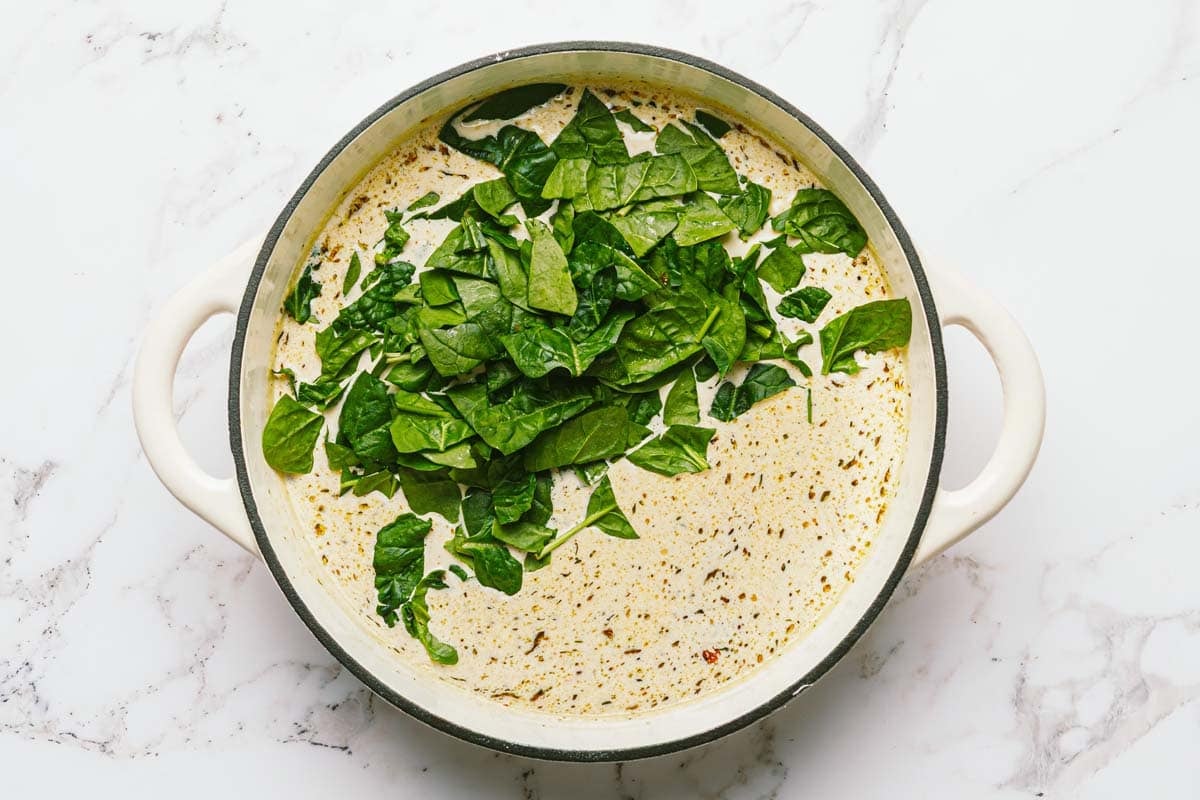 Large pan filled with creamy sauce and fresh spinach. 
