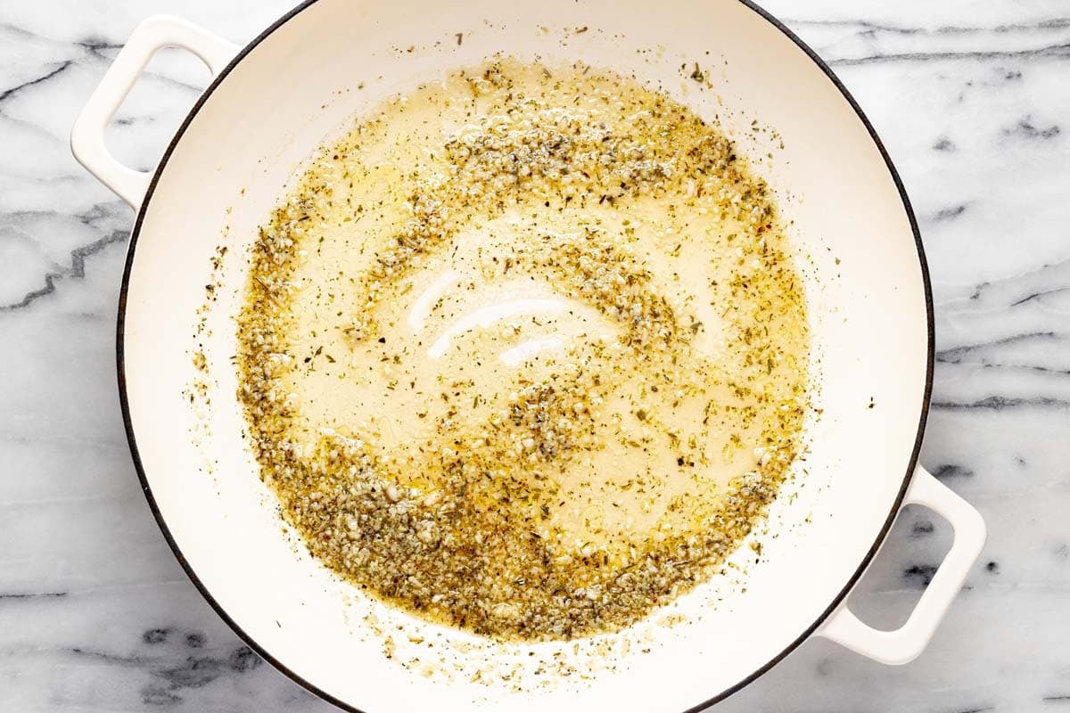 Large pan filled with sauteed garlic and herbs. 