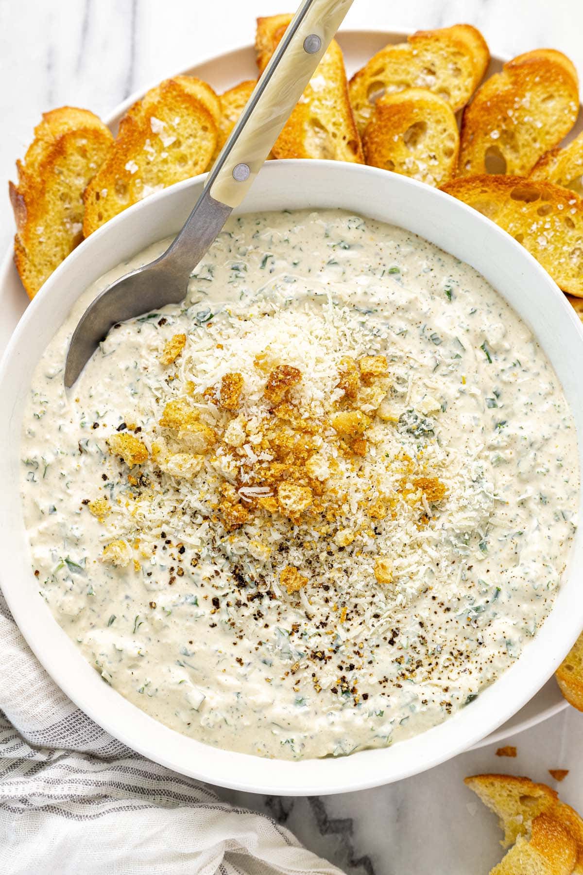 Bowl of Caesar salad dip on a plate of crostini. 
