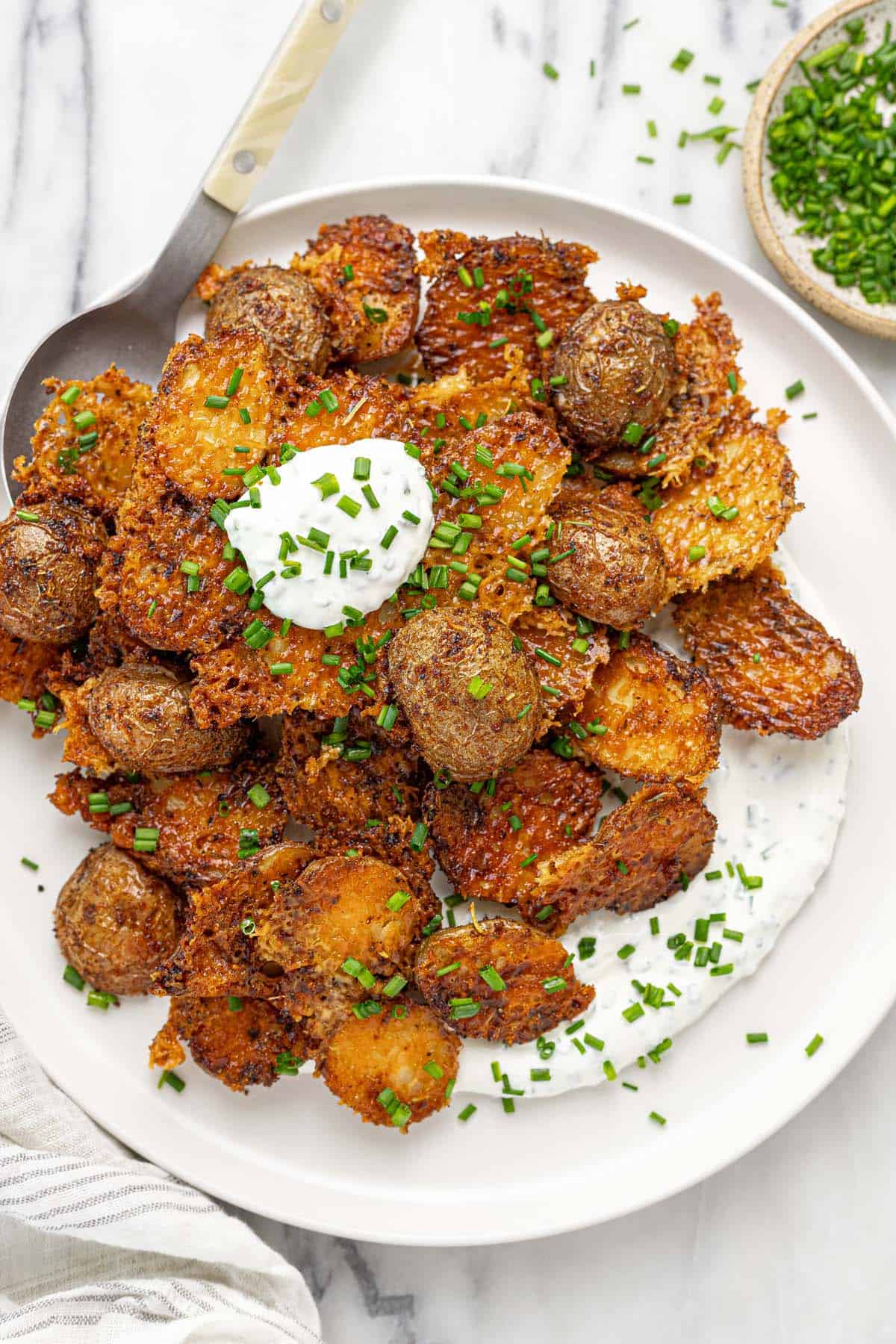 Plate of crispy Parmesan potatoes topped with chives and sour cream. 