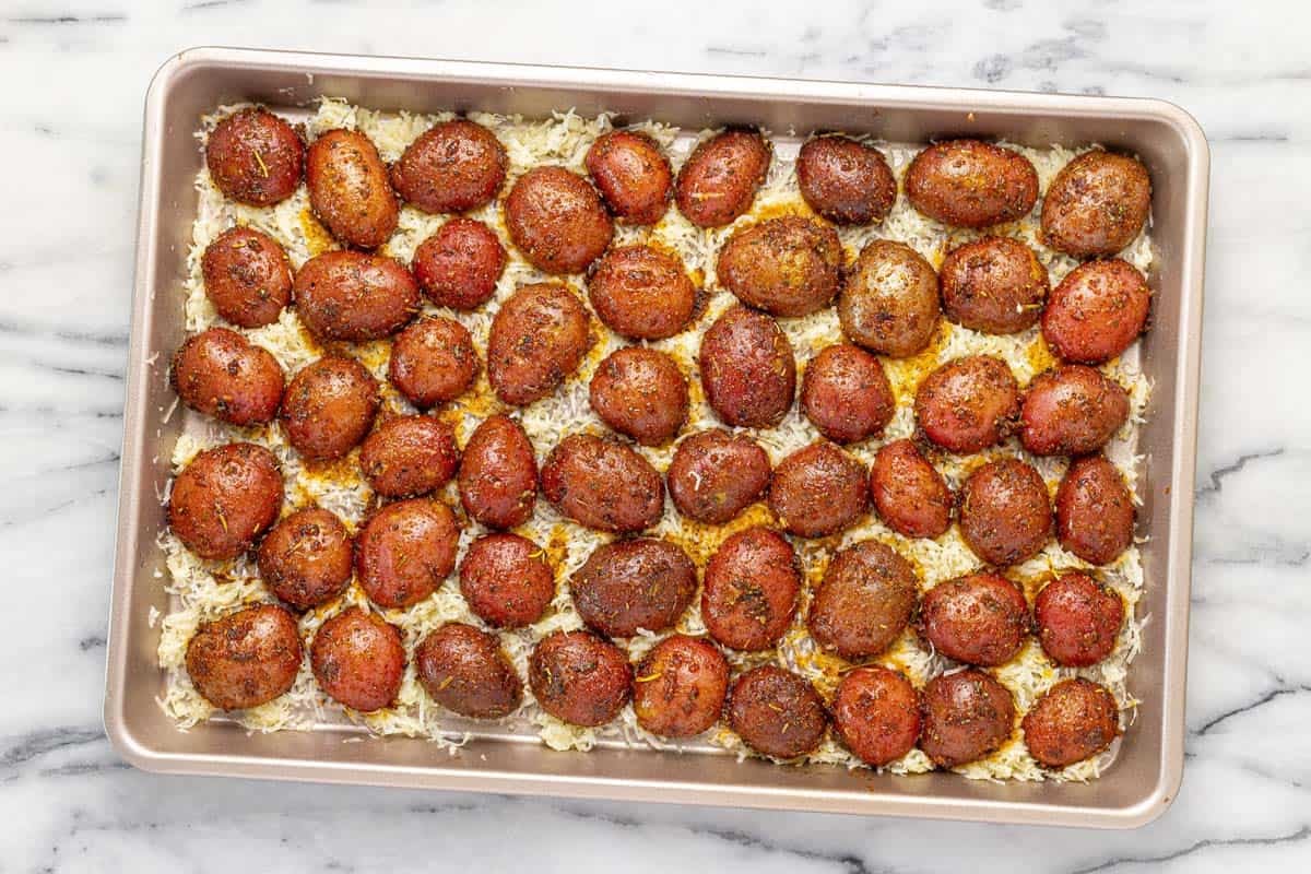 Seasoned potatoes on a bed of Parmesan and butter on a baking sheet. 