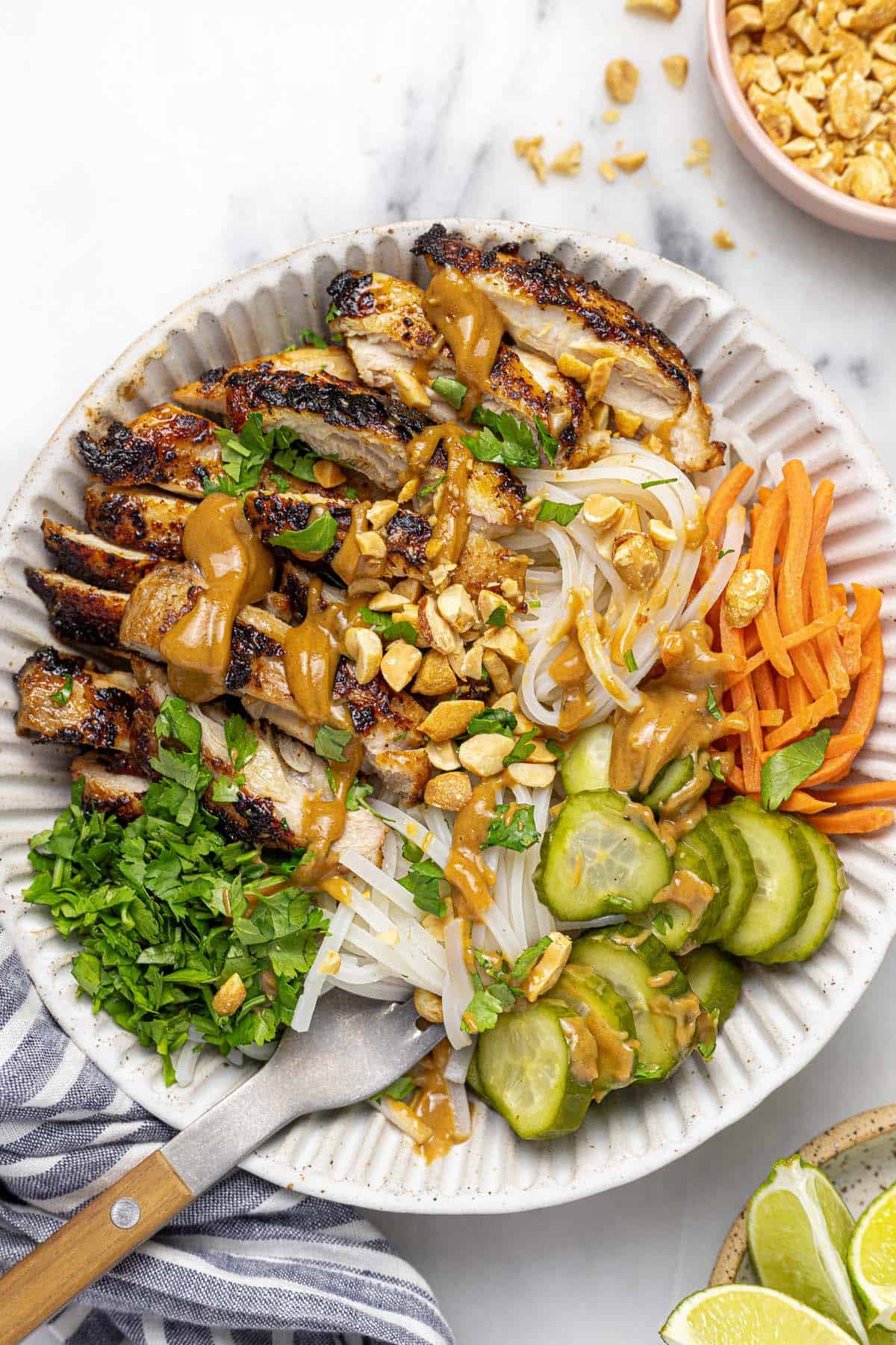 Bowl filled with grilled chicken, noodles, veggies, and peanut sauce. 