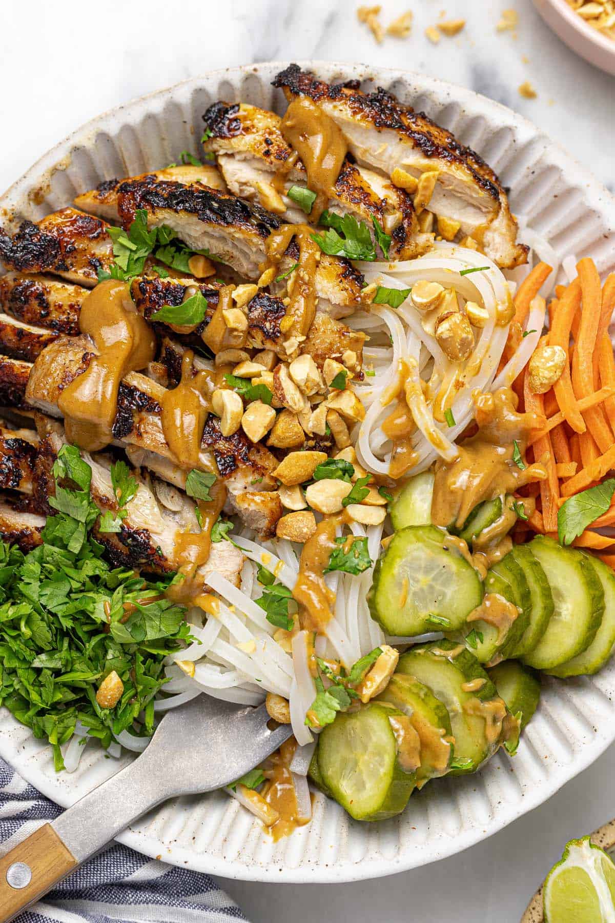 Bowl filled with grilled chicken, noodles, veggies, and peanut sauce. 