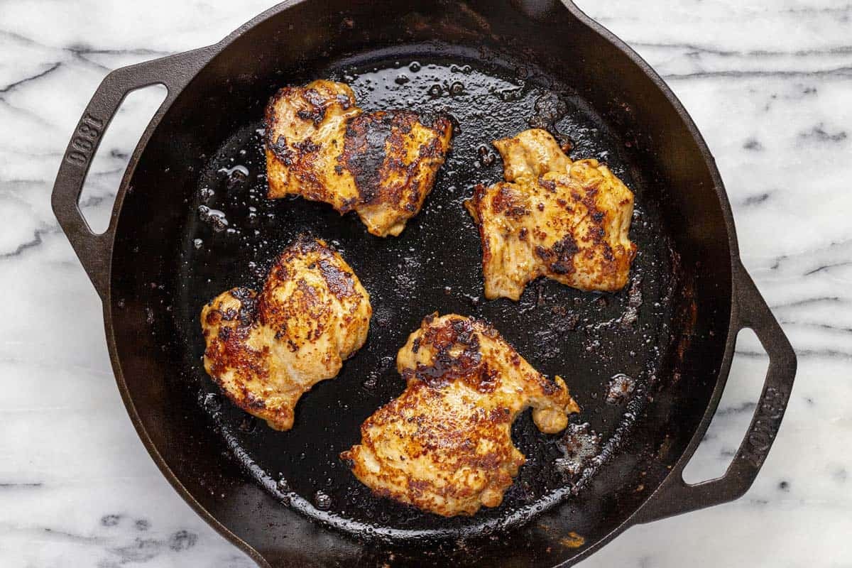 Cooked chicken thighs in a large cast iron skillet. 