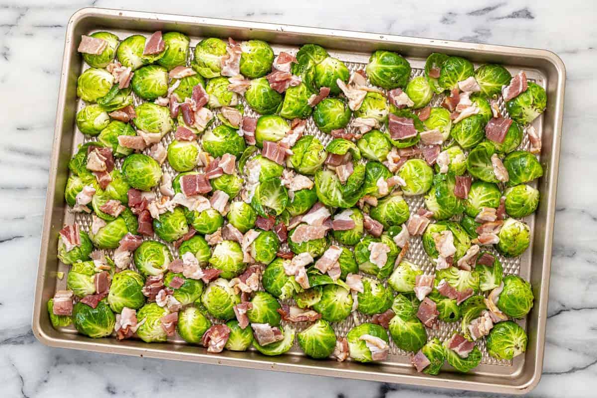 Sheet pan filled with halved Brussels sprouts and diced raw bacon.