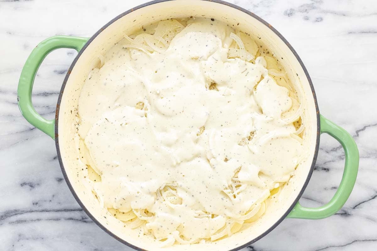 Creamy cheese sauce over sliced potatoes and onions in a pan. 