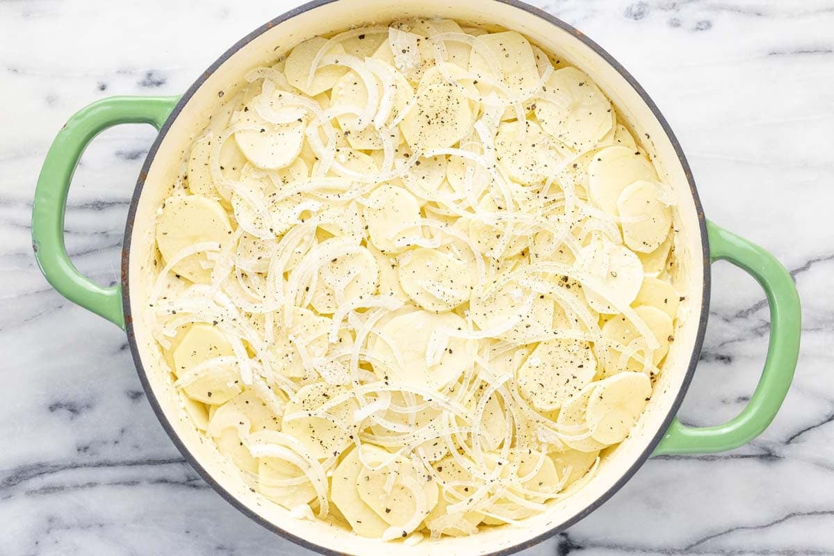 Another layer of sliced potatoes and onions in a large pan. 