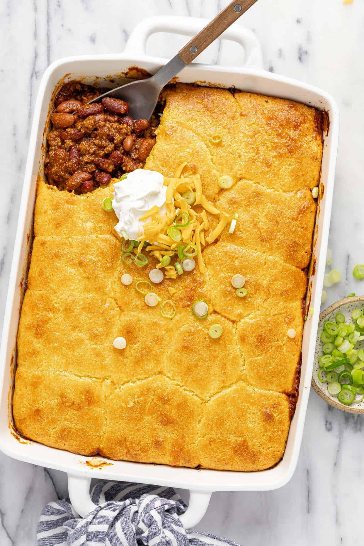 Large baking dish filled with chili and cornbread casserole topped with sour cream, cheese, and green onion. 