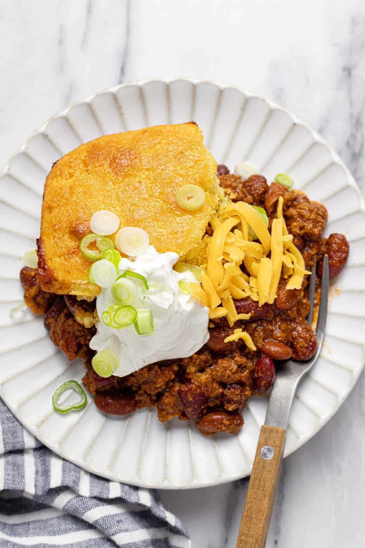 Plate with a sliced of chili cornbread casserole topped with sour cream, cheese, and green onion. 