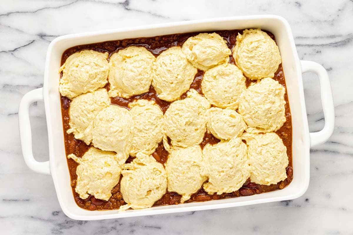 Scoops of cornbread batter on top of a pan of chili. 