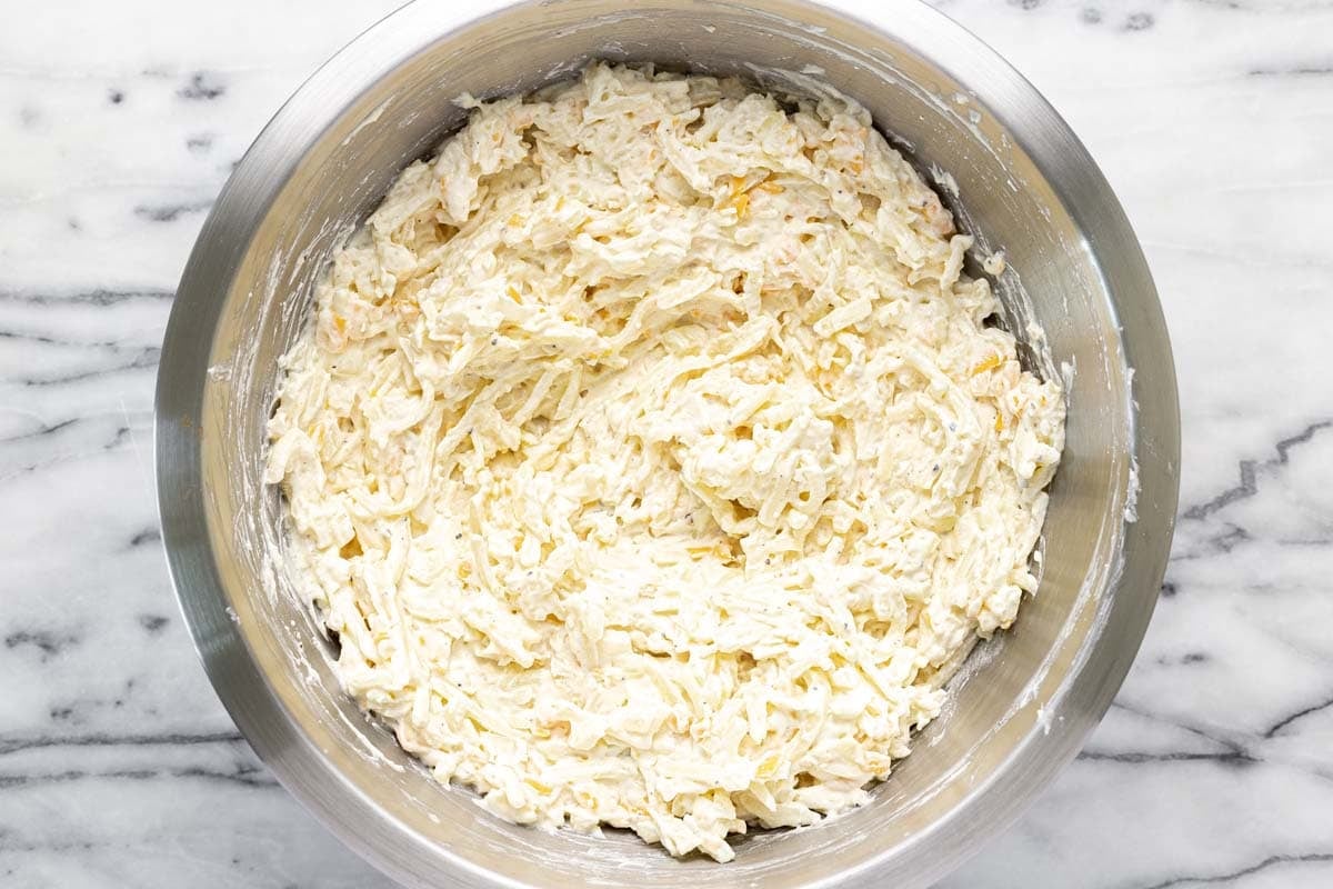Cheesy hashbrown casserole mixed together in a big bowl. 