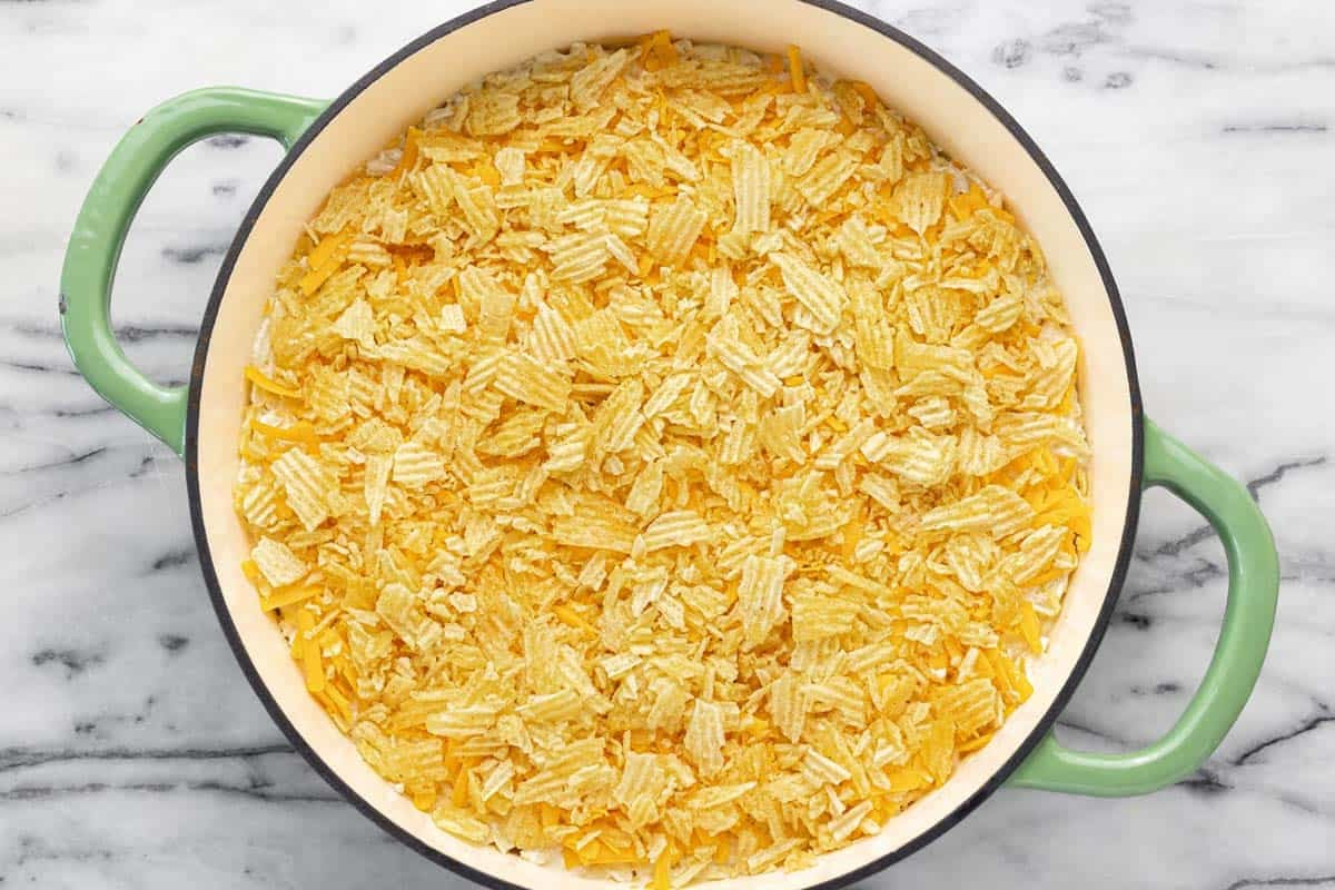 Cheesy hashbrown casserole topped with cheese and potato chips in a large pan. 