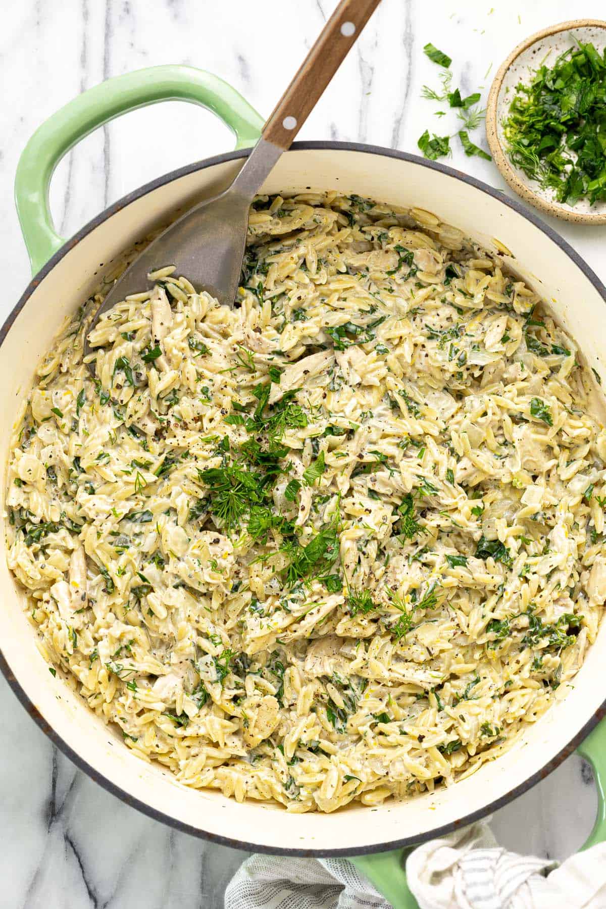 Large pan filled with lemon chicken orzo pasta garnished with fresh herbs. 